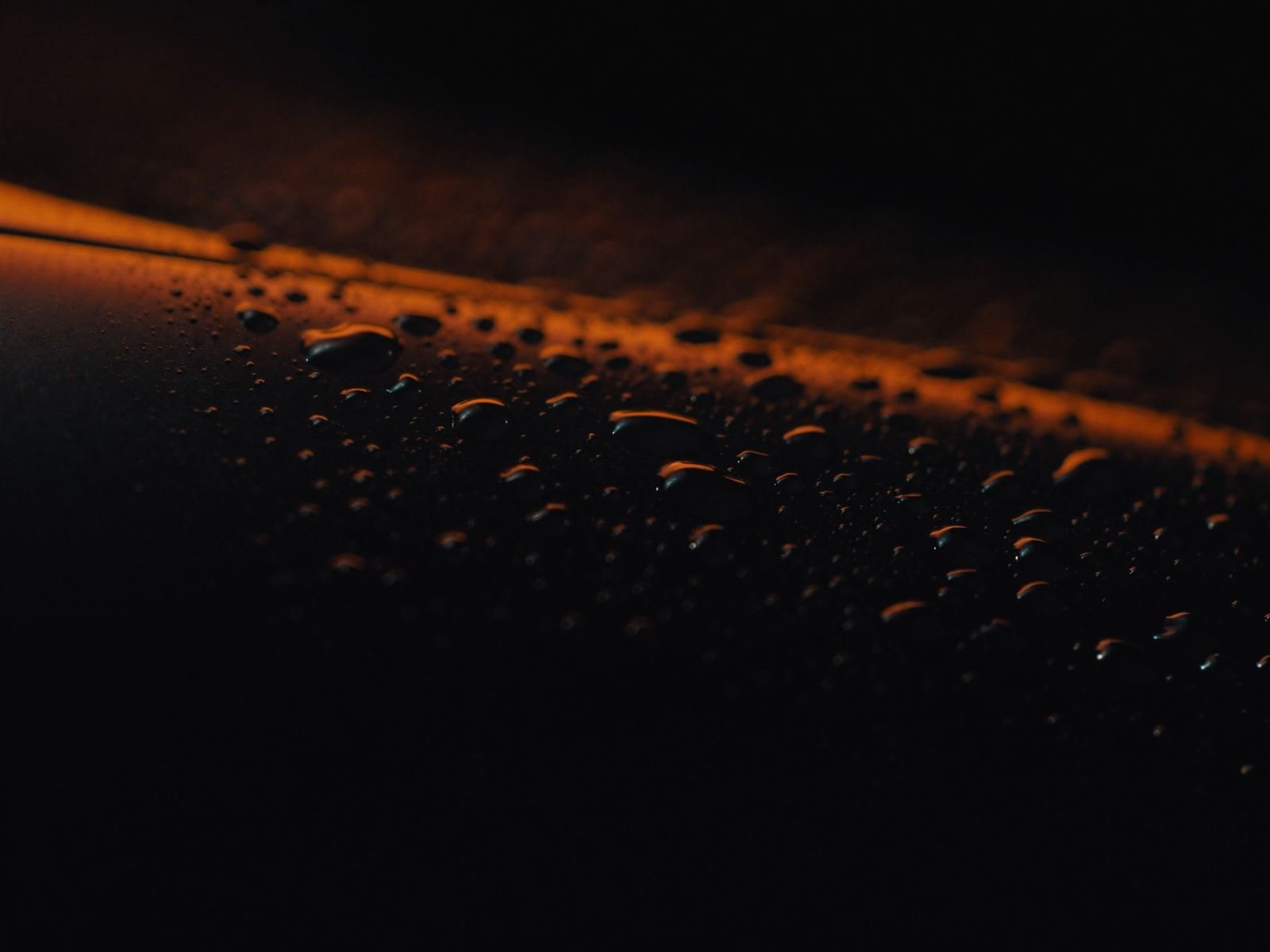 Water beads on black car paint catching orange light