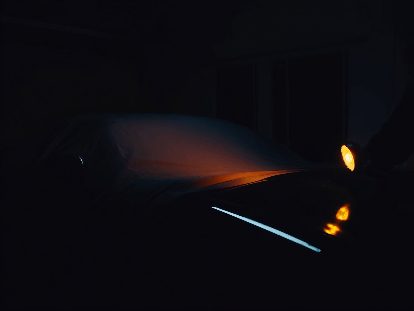 Half-uncovered sports car in a dim garage under an inspection light