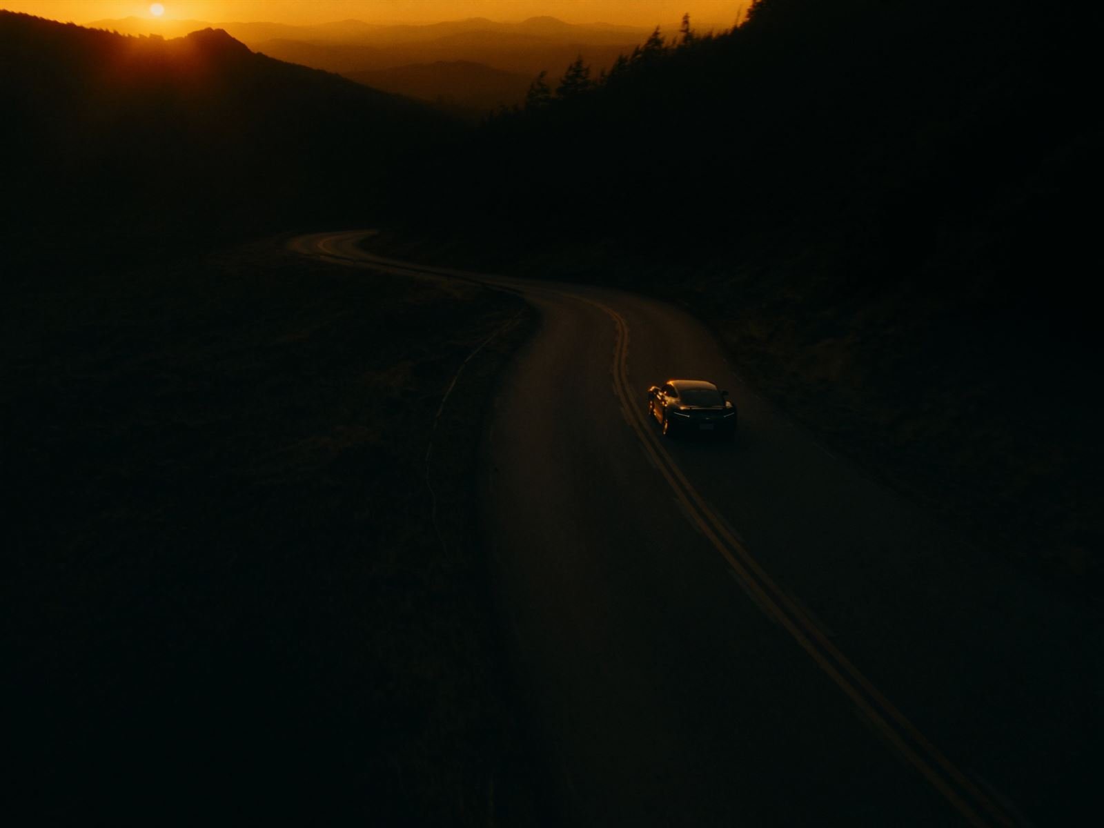 Lone car on a winding mountain road at dusk